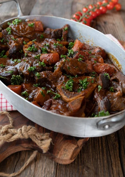 Sunday or holiday meat dish with oven braised beef shanks or beef leg slices with delicious brown gravy in a rustic roasting pan isolated on wooden table