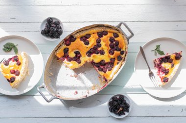 Lezzetli Alman pastası, böğürtlenli ve kremalı puding soslu. Yukarıdan beyaz ahşap masa arkaplanında yemeye hazır..