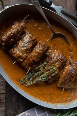 Tahta masaya izole edilmiş rustik kızartma tavasında kahverengi soslu sığır eti Roulades. Üst görünüm