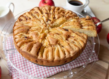 Elmalı turta, bir fincan kahve ve taze elmayla ahşap bir masada.