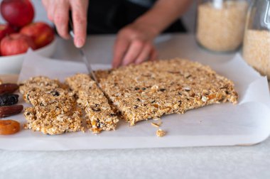 Taze ve ev yapımı granola bar veya kuru meyveli müsli bar, araranth, kinoa, yulaf ve badem mutfak tezgahında bir kadın eli tarafından kesilir. Yakın çekim, ön görünüm