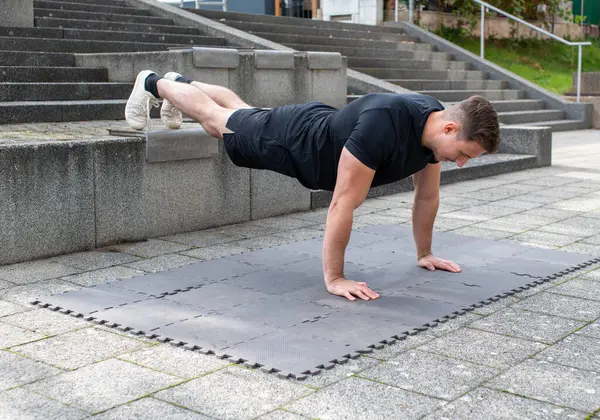Young man doing a decline push-up or elevated push-up on concrete background outdoors
