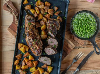 Fırında patatesli domuz filetosu ve ahşap bir masada yeşil bezelye..