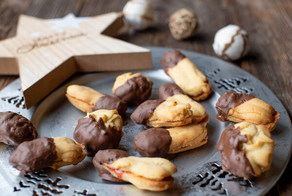 Traditional german shortbread butter cookies, Spritzgebck coated with delicious milk chocolate glaze on a silver christmas plate on decorated wooden table background. closeup