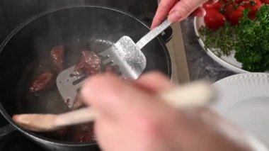 Gulaş, ocakta bir tencerede kızarıyor. Kadınların eli eti çıkarıyor ve kızartma tavasına taze çiğ et koyuyor.