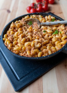 Domates soslu ve kabuklu erişteli lezzetli kremalı ton balığı. Tahta bir kaşıkla, arka planda hafif bir tahta masada yemek için hazır bekliyor. Kopyalama alanı ile dikey yakın çekim.