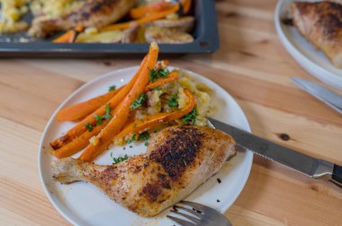 Fırından taze pişmiş fırın, fırında pişmiş tavuk budu, havuç çubuğu ve ezilmiş patates. Çatal ve bıçakla tabakta yemeye hazır. Koyun yemeği