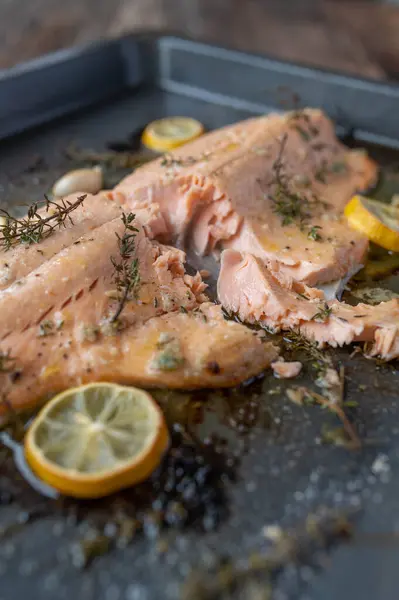Delicious oven baked half salmon fillet with lemon, thyme, garlic and olive oil marinated. Served ready to eat with cross section view on a baking sheet. Closeup