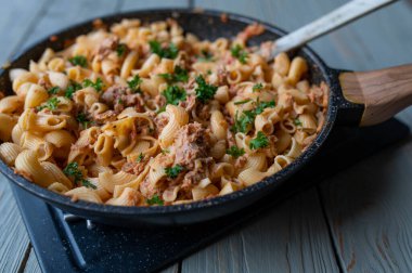 Lezzetli kremalı domates soslu parmesan peynirli ton balığı ve makarna ile lezzetli kolay ve hızlı bir yemek. Tenha bir masada garnitürlü bir tavada servis edilir..