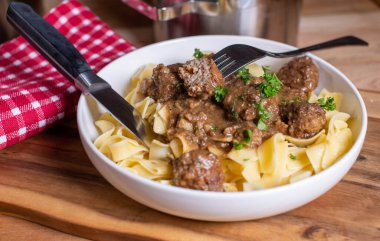 Lezzetli kahverengi mantar soslu köfteli makarna menüsü. Kırsal ve ahşap masa arka planında çatal bıçak takımlarıyla servis ediliyor..