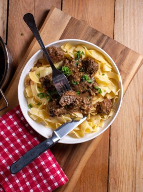 Lezzetli kahverengi mantar soslu köfteli makarna menüsü. Kırsal ve ahşap masa arka planında çatal bıçak takımlarıyla servis ediliyor..