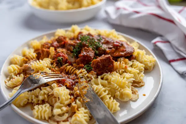Delicious pasta and meat dish with cubed turkey meat in a delicious and tasty sauce. Served with buttered noodles on a plate with fork and knife on a a table. Closeup