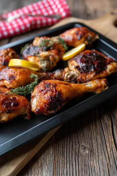 Delicious oven baked barbecue chicken thighs and drumsticks with honey glazed barbecue sauce on a a baking sheet on rustic and wooden table background.