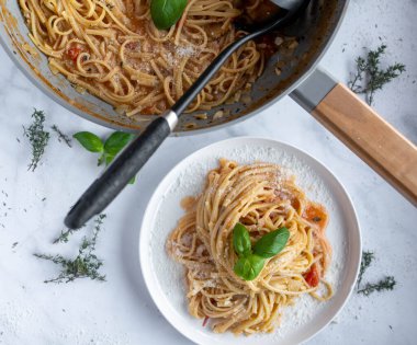 Lezzetli hızlı, kolay ve çabuk makarna ile spagetti, domates, şifalı ot, soğan, sarımsak ve parmesan peyniri. Tavada ve mutfak tezgahında tabakta yemek için hazır bekliyor. Üst görünüm.