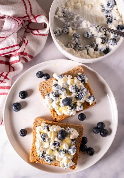High Protein Breakfast with whole grain toast, cottage cheese, blueberries and honey on light kitchen background. Top view