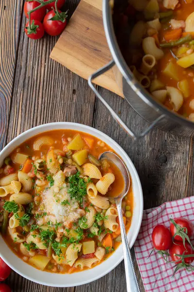 Sebze, fasulye, makarna, pastırma ve parmesan peynirli ev yapımı taze sebze çorbası. Kaşık ve ahşap masa arkasında garnitür..