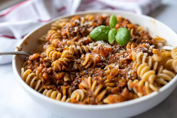 Ev yapımı mercimek bolonez ve fusilli makarna ile nefis vegan yemeği. Mutfak masasının arkasında fesleğen yaprağı olan derin bir tabakta yemeye hazır. Yakın çekim.