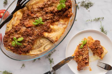 Mozarella ve parmesan peynirli İtalyan gözleme güveci. Bolonez soslu. Güveç kabında servis edilmiş ve arka planda enine kesit manzaralı bir tabakta. Üst görünüm