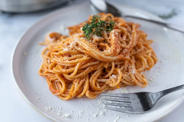 Delicious spaghetti with tomato sauce. Original spaghetti alla pomodoro. Served ready to eat with parmesan cheese on a white plate on light table background.