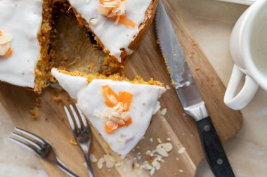 Havuçlu kek, beyaz şekerli, tahta kesme tahtasının üzerinde yukarıdan bıçaklı ve çatallı.