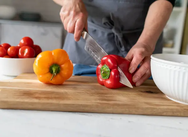 Paprika Mit Einem Küchenmesser Von Frauenhand Auf Einem Schneidebrett Schneiden lizenzfreie Stockbilder