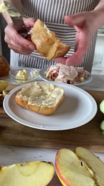 Mutfakta önlüğü olan bir kadın tarafından jambonlu ve salatalıklı sağlıklı bir sandviç ekmeği yapmak.