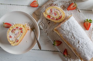 Krem şantili kek rulosu ve beyaz masa arkasında çilek.