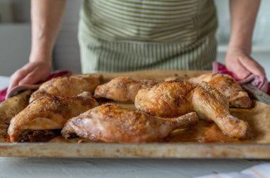 Mutfakta fırında pişmiş tavuk bacağı servis eden bir kadın. Yakın plan, ön görünüm