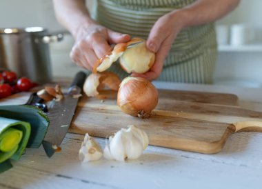 Mutfaktaki kesme tahtasına soğan soyan biri.