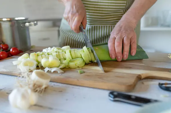 Cutting leek on a cutting board by womans hand in the kitchen.