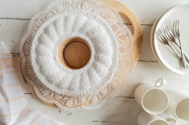 Açık arkaplanda pudra şekerli tam ve kesilmemiş kek.