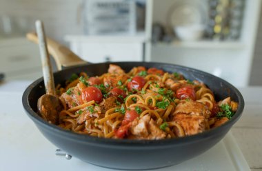 Pan fried salmon with creamy tomato sauce an spaghetti in a skillet on kitchen counter. Ready to eat