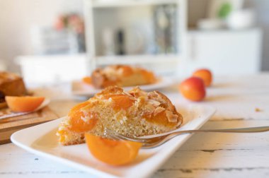 Mutfak arka planında çatallı beyaz bir tabakta taze pişmiş kayısı keki.