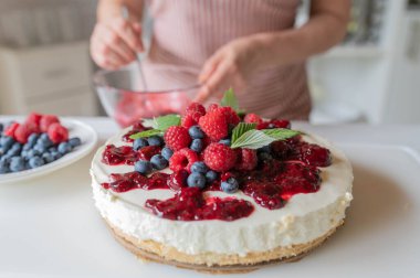 Mutfak tezgahında böğürtlen soslu fırında cheesecake yok. Önlüklü bir kadın tarafından hazırlanıyor.