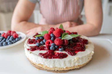 Mutfak tezgahında böğürtlen soslu fırında cheesecake yok. Önlüklü bir kadın tarafından hazırlanıyor.