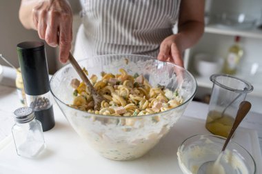 Kadın mayonez, bezelye, sosis ve turşulu taze makarna salatası hazırlıyor.