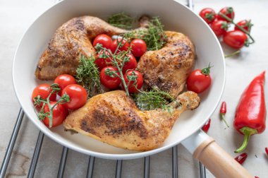 Baked chicken legs with cherry tomatoes and fresh thyme in a frying pan on light kitchen counter background clipart