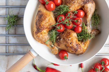 Baked chicken legs with cherry tomatoes and fresh thyme in a frying pan on light kitchen counter background clipart