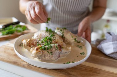 Woman sprinkling chopped parsley over a fresh and homemade cooked dinner with turkey roulades in a cream sauce. clipart