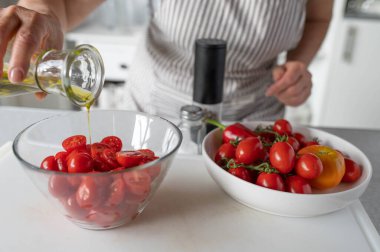 Mutfakta kadınların elleriyle taze ve yarım kiraz domatesli bir kaseye zeytinyağı dök.