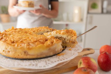 Mutfakta önlüklü bir kadının sunduğu pudingli taze elmalı kek.