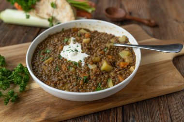 Sağlıklı vejetaryen mercimek çorbası ya da ahşap masa arkasında ekşi kremalı mercimek yahnisi.