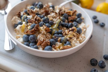 Sağlıklı protein kahvaltı kasesi, süzme peynir, yulaf, ceviz, yabanmersini ve bal.