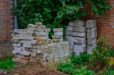 Yığınla inşaat tuğlası ve beton bloklar yeşil arka bahçedeki tuğla bir duvarın yanına yerleştirilmiş..