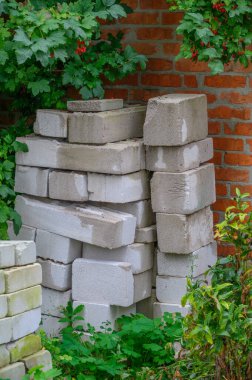 Yığınla inşaat tuğlası ve beton bloklar yeşil arka bahçedeki tuğla bir duvarın yanına yerleştirilmiş..