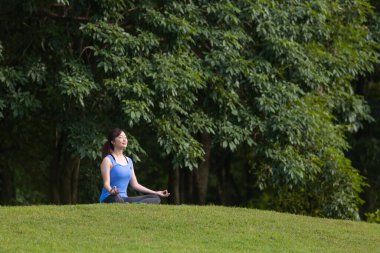 Yoga kıyafetli genç Asyalı kadın iç huzurundan mutluluk elde etmek için ormanda rahatça meditasyon yapıyor. Nefes alma egzersizi, sağlıklı akıl ve ruh sağlığıyla ilgili bilgelik.