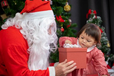 Beyaz bebek Noel Baba 'dan hediye alıyor. Noel kutlaması konsepti için süslenmiş Noel ağacının yanında.