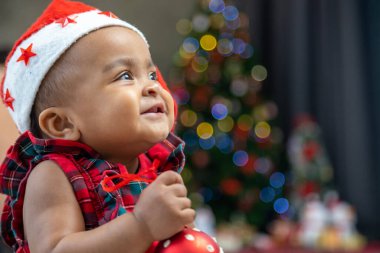 Afro-Amerikan bebek mutlu bir şekilde gülümsüyor. Noel elbisesi ve Noel Baba şapkası giyerken süs eşyalarıyla oynuyor.