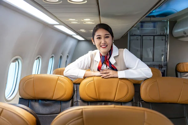 Asian flight attendant posing with smile inside aircraft for welcoming passenger on board with seat on the background for airline travel