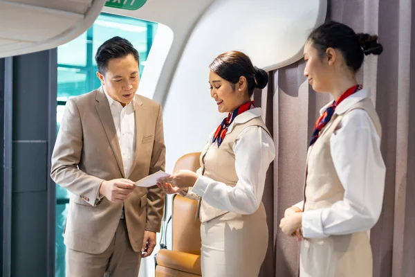 Asian flight attendant is welcoming and checking passenger boarding pass in business class and show the way to his seat for airplane flight and airline transportation